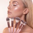 Blonde model with glowing, dewy makeup look holding the complete 5-piece Beauty by Bella makeup brush collection